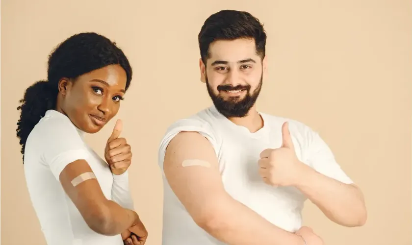 Two smiling adults giving a thumbs-up, showing bandages on their arms after getting vaccinated